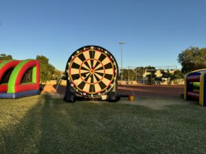 Kids and adults kick soft Velcro soccer balls at a giant inflatable soccer darts dartboard with a large bullseye target.